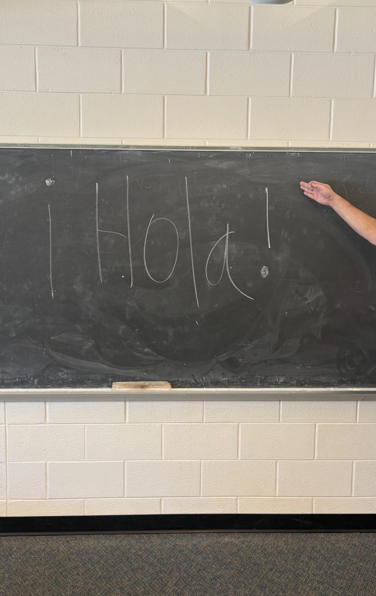 A person pointing to the word Hola on the board, in classroom U4
