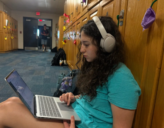 Student Rachel Kraus '28 pictured in the hallway, doing work with headphones on during her free time.